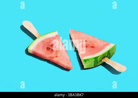 Due zeppe di anguria, disegnate come posacchettine, proiettano lunghe ombre su sfondo blu brillante, rinfresco estivo, design minimalista del cibo Foto Stock