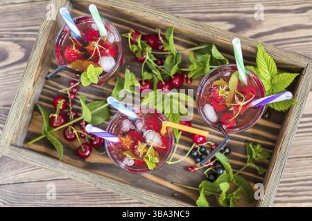 Tre bicchieri di bevanda rinfrescante aromatizzata con frutta fresca in una scatola di legno circondata da frutta. Vista dall'alto. Sfondo in legno Foto Stock