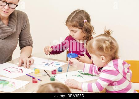 I bambini e i tutor sono la verniciatura con un pennello e acquerelli su carta nella scuola materna Foto Stock