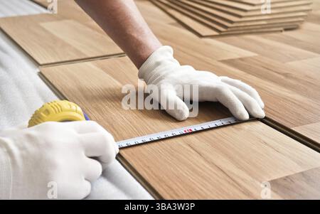 Installazione di pavimenti laminati, dettagli sulle mani dell'uomo con guanti bianchi che reggono il metro su piastrelle di legno, Liptovsky Mikulas, Slovacchia, Europa Foto Stock
