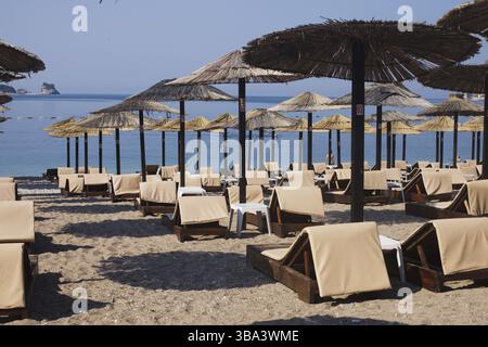 File di sedie a sdraio in legno marrone e ombrelloni in paglia sulla spiaggia di mare al mattino. Budva, Montenegro, Europa Foto Stock
