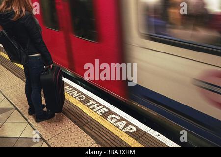 Londra, Regno Unito - 01 febbraio 2019: Ragazza con la sua valigia nera in attesa alla stazione metropolitana di Londra, in quanto il treno sta arrivando dietro il lin giallo Foto Stock