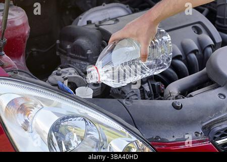 Uomo che versa acqua distillata alternativa ecologica al liquido di lavaggio al serbatoio del lavavetri in auto, dettaglio a portata di mano che tiene flacone in plastica trasparente, Liptovsky Miku Foto Stock