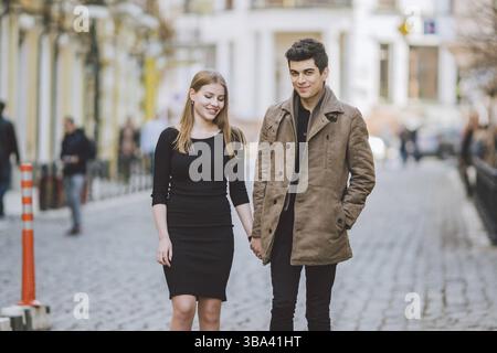 Moderno urbano giovane amore giovane passeggiate romantiche parlando di parlare tenendo le mani su una data. I giovani turchi multiculturale bruna e Caucasico giovane su Foto Stock