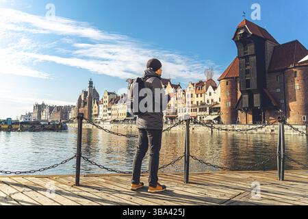 Tema del turismo in Polonia. Viaggio a Danzica. Un viaggiatore maschile utilizza un telefono sull'argine del fiume Motlawa in mezzo all'attrazione principale, un simbo Foto Stock