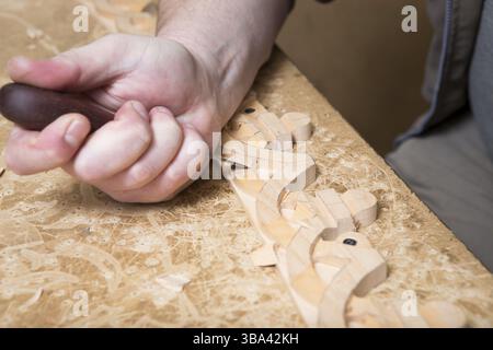 L'intagliatore artigianale crea un ornamento di mobili. Mani, scalpelli, utensili, ornamenti intagliati in legno Foto Stock