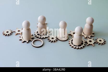 Un'immagine concettuale con figure di legno in piedi su ingranaggi interconnessi. Lavoro di squadra, collaborazione e la natura interconnessa del concetto di lavoro. Foto Stock