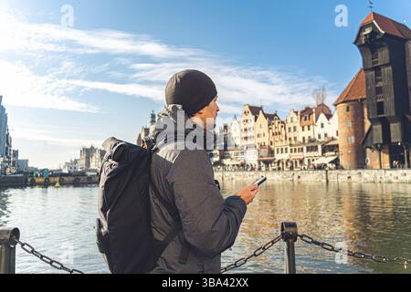 Tema del turismo in Polonia. Viaggio a Danzica. Un viaggiatore maschile utilizza un telefono sull'argine del fiume Motlawa in mezzo all'attrazione principale, un simbo Foto Stock