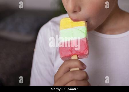 Le mani dei bambini tengono in mano un gelato multicolore e mangiano un gelato Foto Stock
