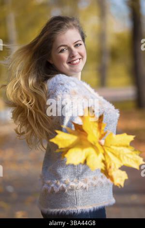 Bella giovane donna con foglie gialle nel parco autunnale Foto Stock