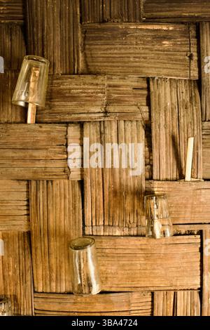 I bicchieri di vetro sono appesi capovolti da una parete di bambù intrecciata all'interno di una capanna tribale Tripura nell'area di Bandarban, Chittagong Hill Tracts. Foto Stock