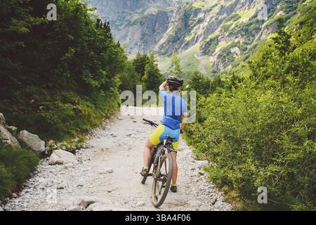 La ragazza in bicicletta viaggia in Slovacchia. Casco nero, camicia blu, montagne, alti Tatra, clima soleggiato Foto Stock