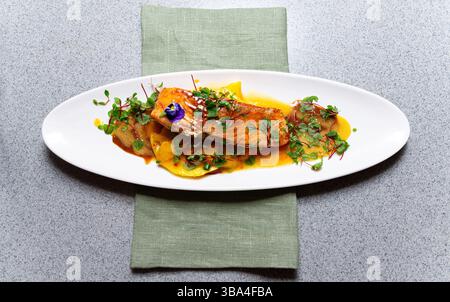 Vista dall'alto di un piatto gourmet di salmone servito con salsa di mango, decorato con microgreen e una decorazione commestibile di fiori viola. Foto Stock