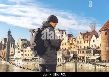 Tema del turismo in Polonia. Viaggio a Danzica. Un viaggiatore maschile utilizza un telefono sull'argine del fiume Motlawa in mezzo all'attrazione principale, un simbo Foto Stock