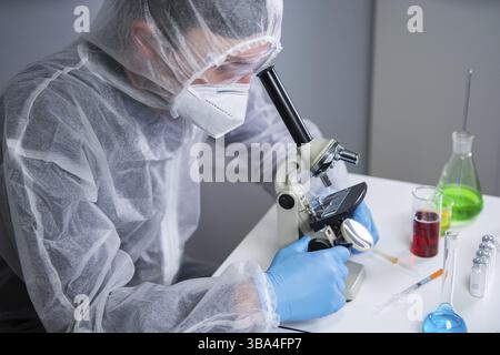 Scienziato che esamina il campione con un microscopio, facendo ricerca medica in laboratorio di scienza. Assistente di laboratorio maschile nello studio degli indumenti protettivi Foto Stock