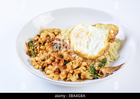 Calamari saltati piccanti con foglie di basilico e peperoncino, uova con il lato soleggiato, servite con riso integrale. Piatto caldo e piccante Foto Stock