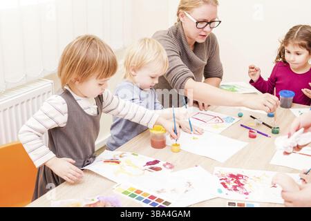 I bambini e i tutor sono la verniciatura con un pennello e acquerelli su carta nella scuola materna Foto Stock