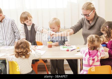 I bambini e i tutor sono la verniciatura con un pennello e acquerelli su carta nella scuola materna Foto Stock