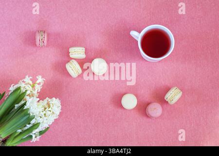 Splendido sfondo per le vacanze primaverili. Tazza di tè, biscotti freschi di Giacinto bianco e bacche dolci e macaron alla vaniglia su un terreno di copiatura rosa Foto Stock
