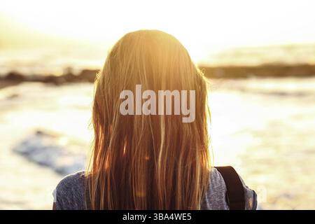 Una giovane donna guarda il mare durante il tramonto. Vista dal retro, dettagli solo sui suoi capelli, Lapta, Cipro, Europa Foto Stock
