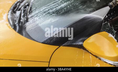 Dettaglio del finestrino anteriore giallo dell'auto lavato in autolavaggio, spruzzatura dell'acqua dall'ugello ad alta pressione, Liptovsky Mikulas, Slovacchia, Europa Foto Stock