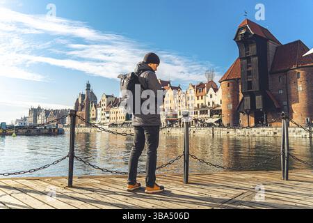 Tema del turismo in Polonia. Viaggio a Danzica. Un viaggiatore maschile utilizza un telefono sull'argine del fiume Motlawa in mezzo all'attrazione principale, un simbo Foto Stock