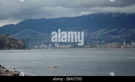 Lions Gate Bridge che collega Vancouver con montagne nuvolose sullo sfondo Foto Stock
