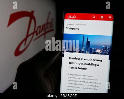 In questa illustrazione fotografica, una persona ha in mano un cellulare con la pagina Web della società danese di HVAC Danfoss sullo schermo davanti al logo. Foto Stock