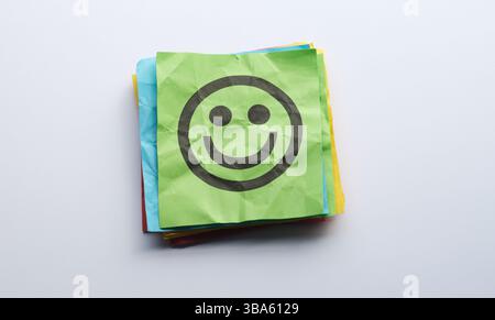 Una pila di note di carta colorate con un volto felice su uno di loro. Primo piano. Foto Stock
