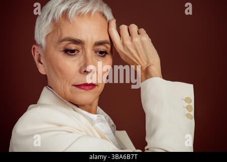 Ritratto di una donna d'affari anziana con un abbigliamento elegante su sfondo marrone che trasuda fascino e professionalità Foto Stock