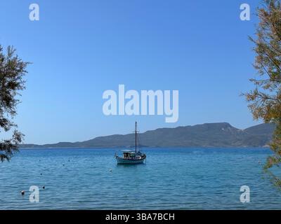 Barca a vela ancorata sulla spiaggia con sfondo montano, Adamantas, Milos, Grecia Foto Stock