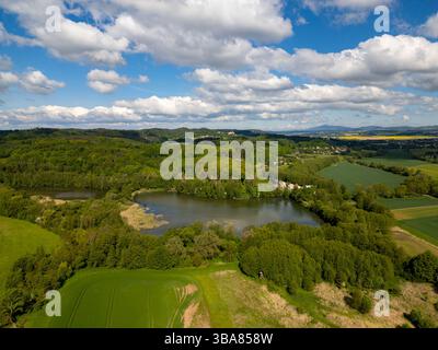 Vista aerea del Rokytnicke rybniky a Hruba Skala, Repubblica Ceca, circondato da verdi foreste e natura tranquilla, che riflette il calmo cielo estivo Foto Stock