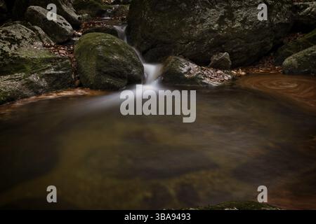 Autunno lunga esposizione del Creek e nero (grande) Stolpich cascate in Jizera Mountain. L'acqua cade in un profondo canyon di foresta piena di pietre di granito Foto Stock