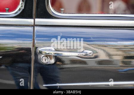 Primo piano della maniglia della portiera cromata su un'auto d'epoca nera. Vista dettagliata della maniglia e della serratura della portiera cromata lucida di un veicolo vintage nero lucido, con Foto Stock