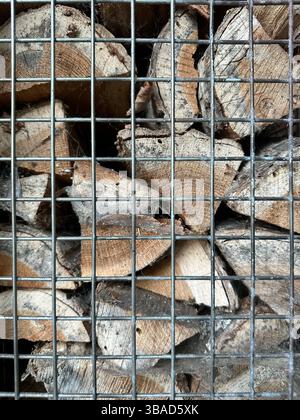 Tronchi di legno tritati impilati in una gabbia metallica d'argento, che mostra gli anelli degli alberi e le trame ruvide della corteccia, ideale per disegni di sfondo o a tema naturale. Foto Stock
