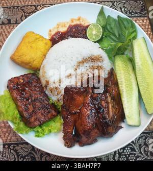 Cibo indonesiano - riso al vapore con Ayam Bakar, Tempe Bacem e Tahu Goreng insieme a verdure crude e sambal di peperoncino rosso Foto Stock