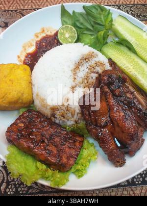 Cibo indonesiano - riso al vapore con Ayam Bakar, Tempe Bacem e Tahu Goreng insieme a verdure crude e sambal di peperoncino rosso Foto Stock