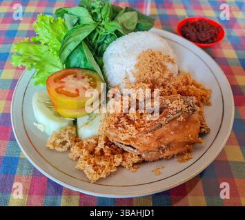Nasi Ayam Goreng e cibo indonesiano di riso al vapore con pollo fritto, verdure crude e sambal piccante di peperoncino rosso. Foto Stock