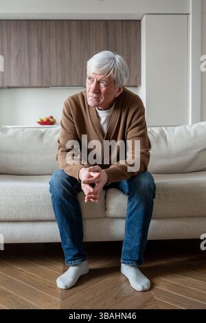 Uomo anziano abbandonato solo si siede perso nel pensiero sul divano con le braccia incrociate, perdita di memoria depressa Foto Stock
