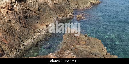 Le onde si infrangono contro rocce torreggianti su un mare aspro, dove il potere della natura incontra la bellezza selvaggia della costa Foto Stock