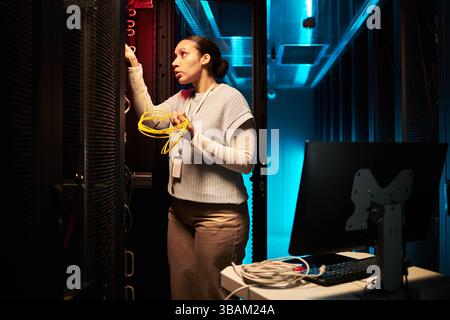 Donna che gestisce con determinazione le apparecchiature della sala server Foto Stock