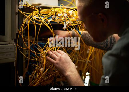 Uomo che verifica i cavi di rete nella sala server Foto Stock