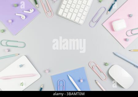 Vista dall'alto di tastiera bianca, mouse, touchpad, custodia per auricolari, penna su sfondo grigio. Quaderni viola, rosa e blu, penne, matite, graffette, spille. Foto Stock