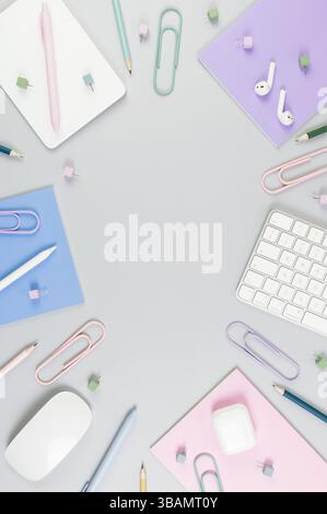 Vista dall'alto di tastiera bianca, mouse, touchpad, custodia per auricolari, penna su sfondo grigio. Quaderni viola, rosa e blu, penne, matite, graffette, spille. Foto Stock