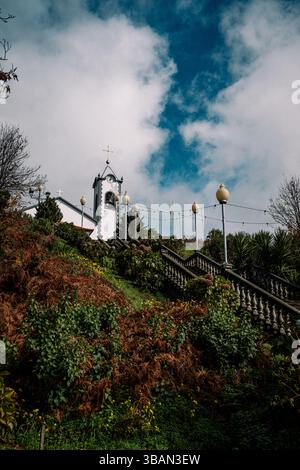 Chiesa bianca con campanile arroccato su una lussureggiante collina verde con scalinata in pietra ornata Foto Stock