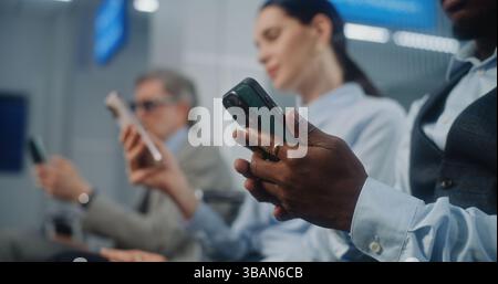 Sala d'imbarco VIP presso il terminal dell'aeroporto internazionale: Persone di lavoro multietniche di successo che utilizzano smartphone, che lavorano online durante un viaggio di lavoro. Squadra imprenditoriale in attesa di volo. Primo piano. Foto Stock