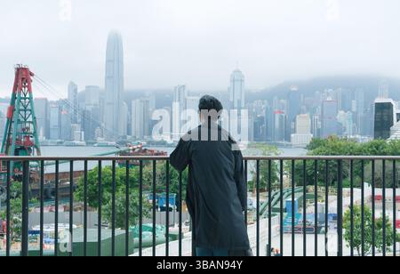 Man osserva Victoria Harbour dallo skyline della città da una terrazza in un pomeriggio nebbioso Foto Stock