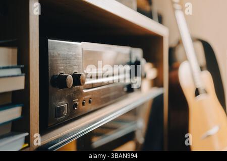 Un amplificatore e un ricevitore come sistema Hi-fi domestico, un vecchio modello su uno scaffale della stanza, una chitarra acustica può essere vista sullo sfondo. Foto Stock