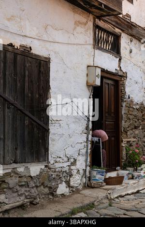 Una porta di legno intemprata posta in un muro di pietra dipinta di bianco a Sirince, che mostra l'architettura rustica del villaggio e il carattere rurale turco senza tempo. Foto Stock