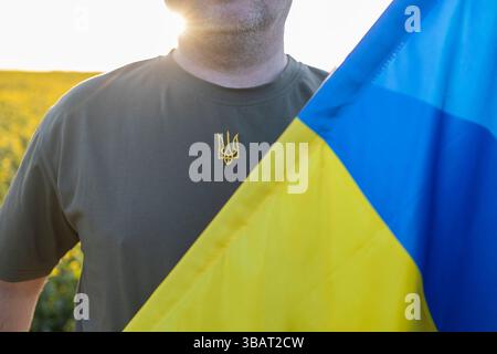 Un uomo irriconoscibile con una T-shirt kaki con tridente ricamato e bandiera blu gialla. State con l'Ucraina. Difendi la patria, la forza di Th Foto Stock